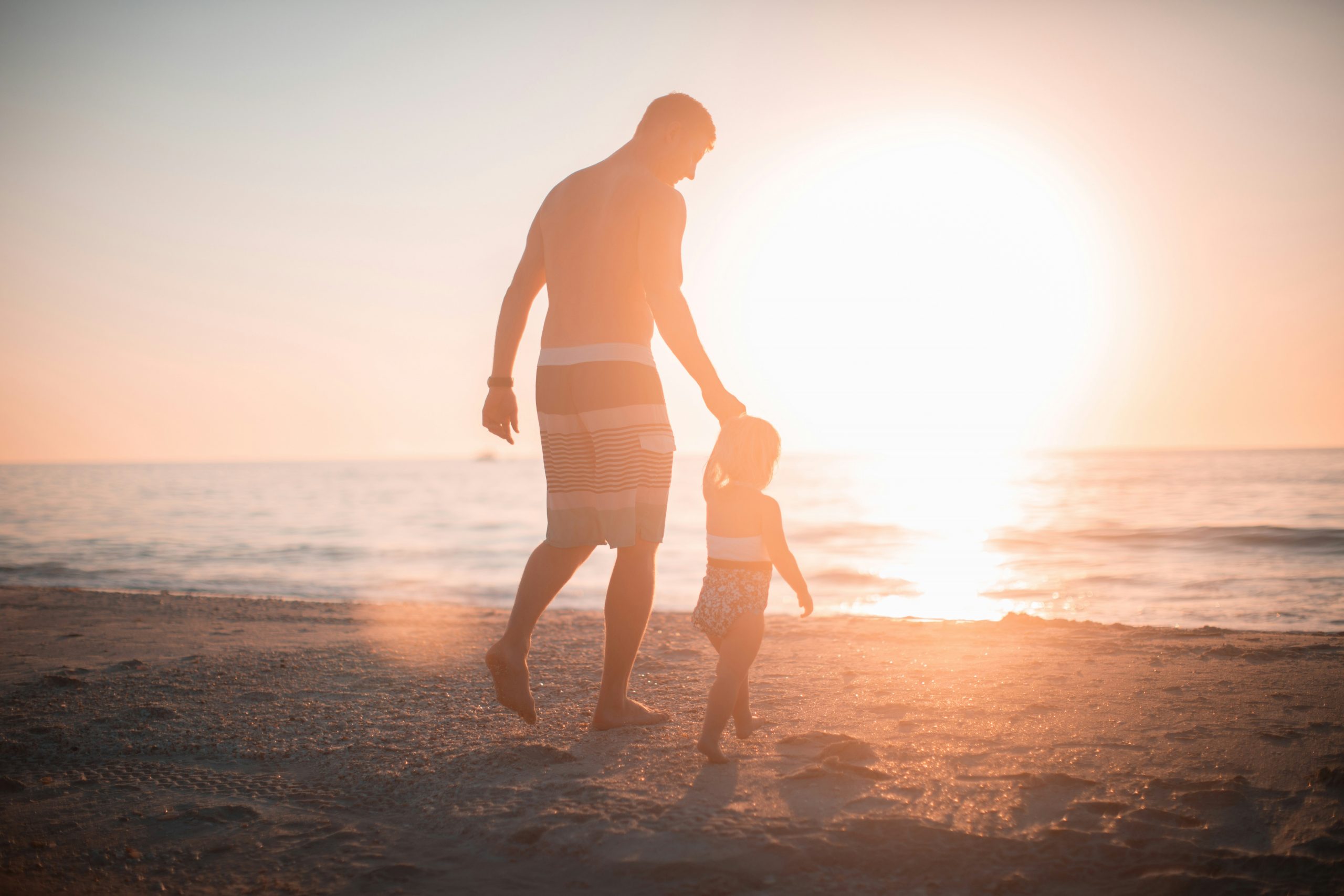 Beach sunrise Parent with child walking along the beach at sunrise