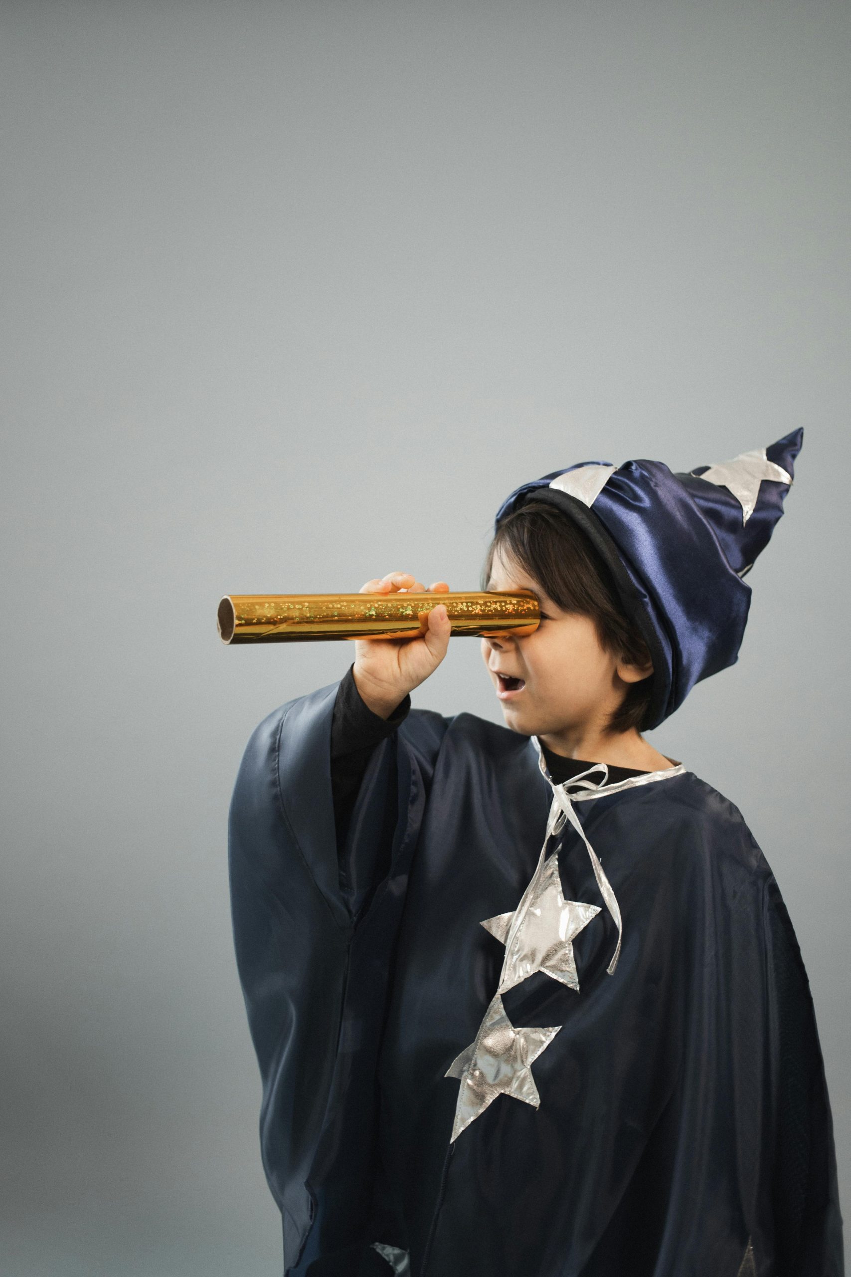 Child in a wizard costume looking through a telescope