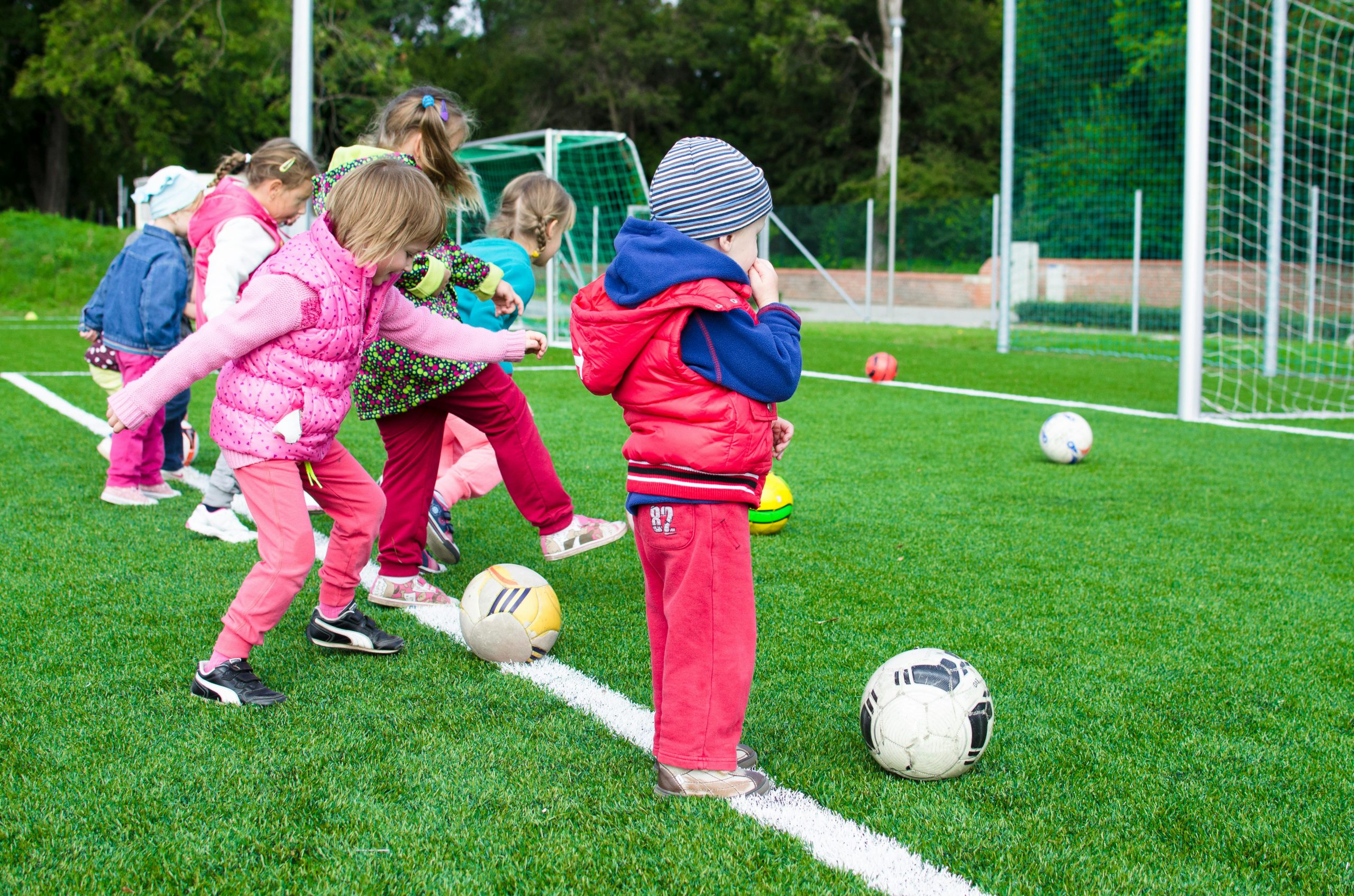 Small children lined up kicking soccer balls toward a goal